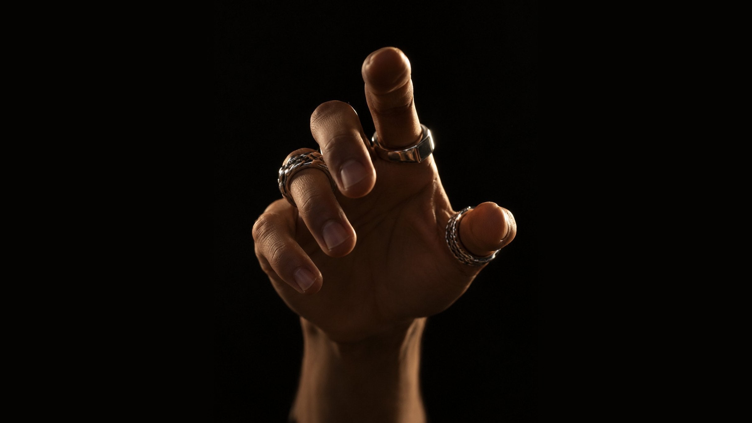 Hand reaching toward the camera wearing three silver rings against black