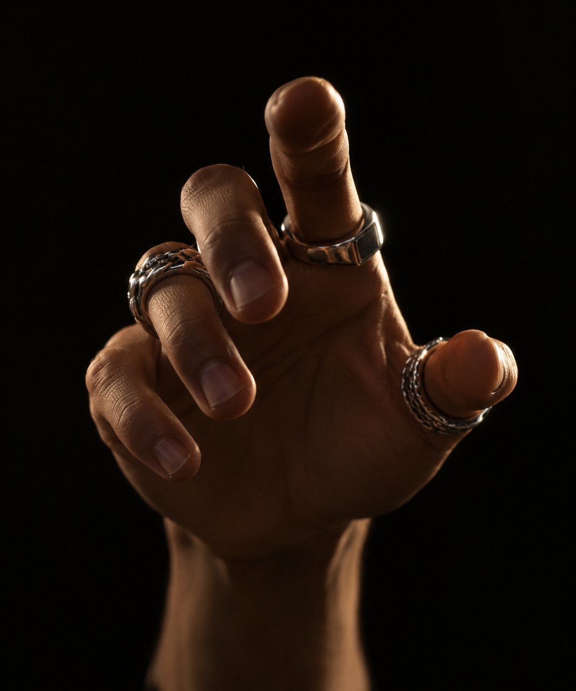 Raised hand wearing three silver rings against black