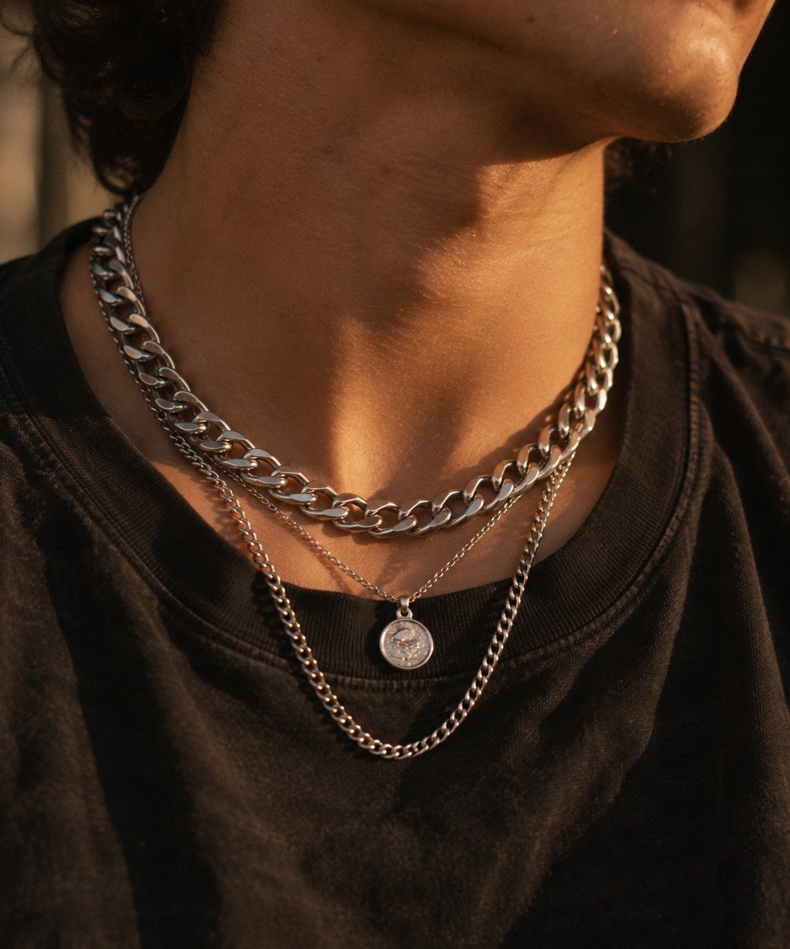 Layered silver curb chains and a coin pendant over a black tee