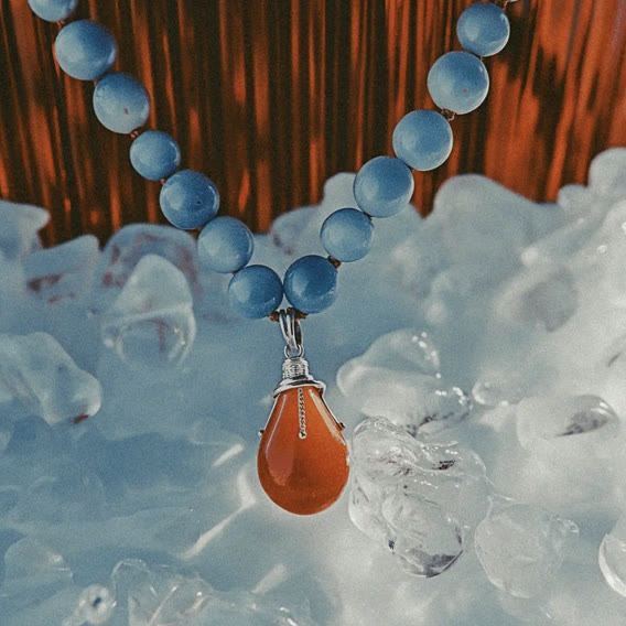 Blue bead necklace with an orange drop pendant on ice
