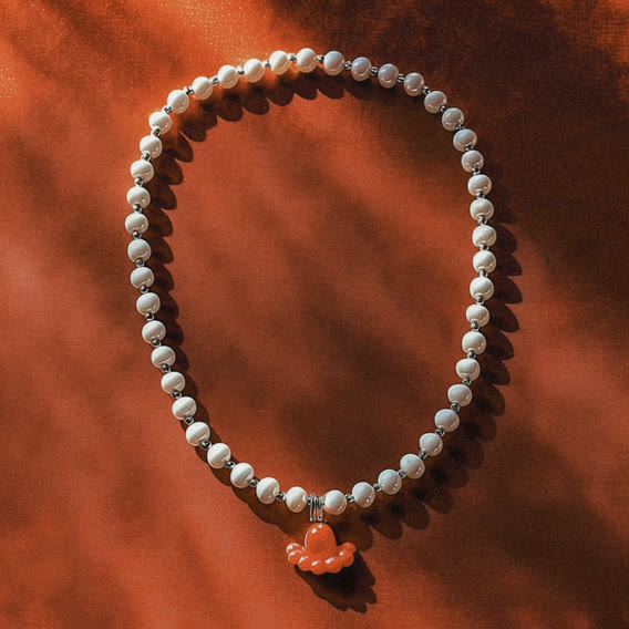 Pearl necklace with a coral charm on orange fabric
